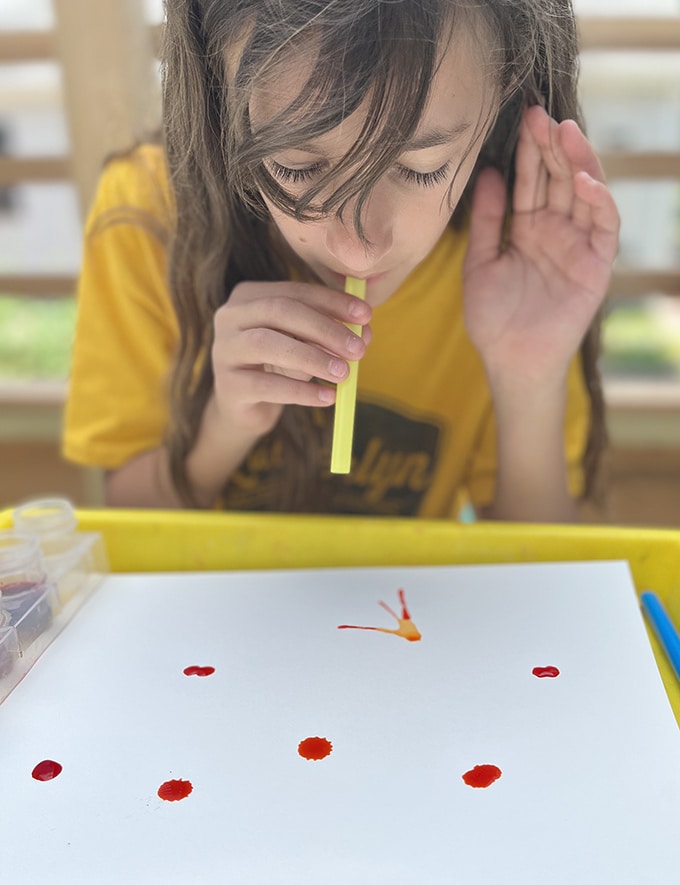 child blowing paint with straws
