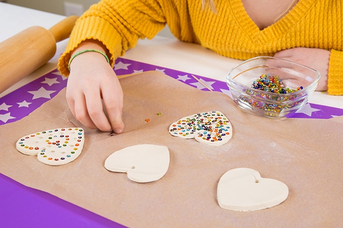 Child decorating air dry clay heart ornaments with beads